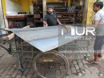 Labourers carry an iron plate to load onto a cycle rickshaw outside a shop at a steel and iron wholesale market in Kolkata, India, on Novemb...