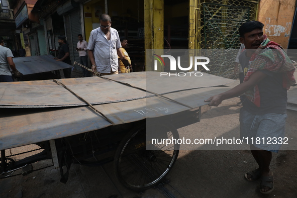 Labourers carry an iron plate to load onto a cycle rickshaw outside a shop at a steel and iron wholesale market in Kolkata, India, on Novemb...