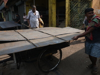 Labourers carry an iron plate to load onto a cycle rickshaw outside a shop at a steel and iron wholesale market in Kolkata, India, on Novemb...