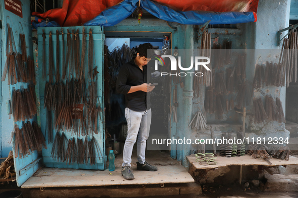 A trader looks at his mobile phone inside his shop at a wholesale steel and iron market in Kolkata, India, on November 26, 2024. In November...