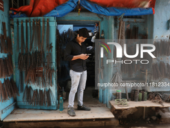 A trader looks at his mobile phone inside his shop at a wholesale steel and iron market in Kolkata, India, on November 26, 2024. In November...