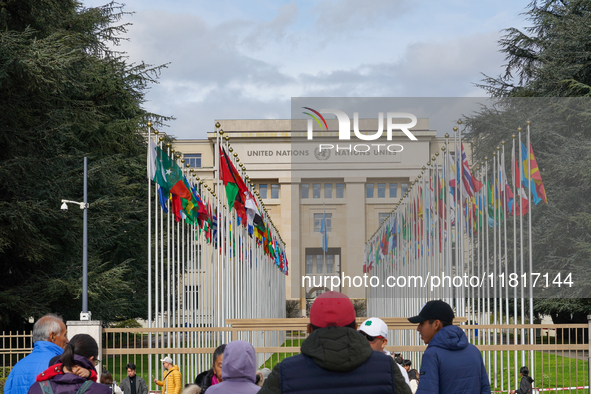 People stand outside the gates of the United Nations building in Geneva, Switzerland, where the flags of member states line the entrance, sy...