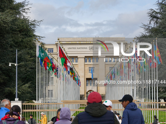 People stand outside the gates of the United Nations building in Geneva, Switzerland, where the flags of member states line the entrance, sy...