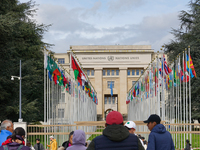 People stand outside the gates of the United Nations building in Geneva, Switzerland, where the flags of member states line the entrance, sy...