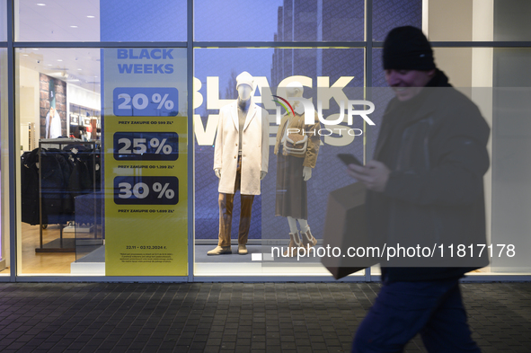 A man carries a box and a smartphone as he walks past a shop window with Black Week sales displayed ahead of Black Friday in Warsaw, Poland,...