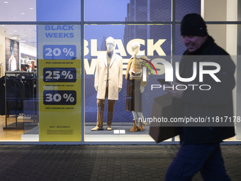 A man carries a box and a smartphone as he walks past a shop window with Black Week sales displayed ahead of Black Friday in Warsaw, Poland,...