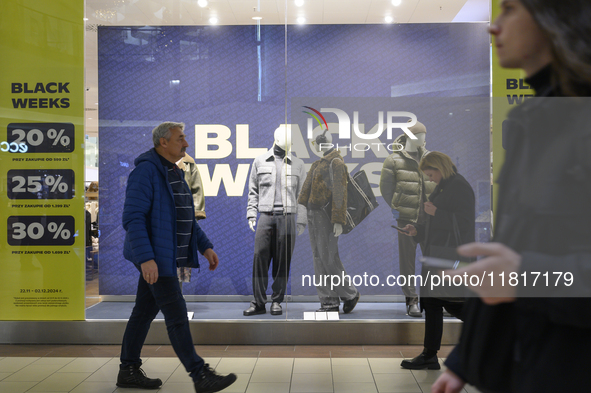 People walk past a shop window with Black Week sales displayed ahead of Black Friday in Warsaw, Poland, on November 28, 2024. 