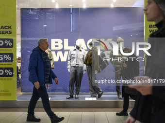 People walk past a shop window with Black Week sales displayed ahead of Black Friday in Warsaw, Poland, on November 28, 2024. (