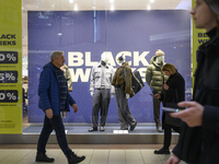 People walk past a shop window with Black Week sales displayed ahead of Black Friday in Warsaw, Poland, on November 28, 2024. (