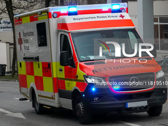 A Bavarian Red Cross ambulance, marked with bright red and yellow reflective panels, responds to an emergency with its blue lights activated...