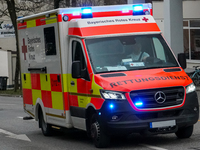 A Bavarian Red Cross ambulance, marked with bright red and yellow reflective panels, responds to an emergency with its blue lights activated...