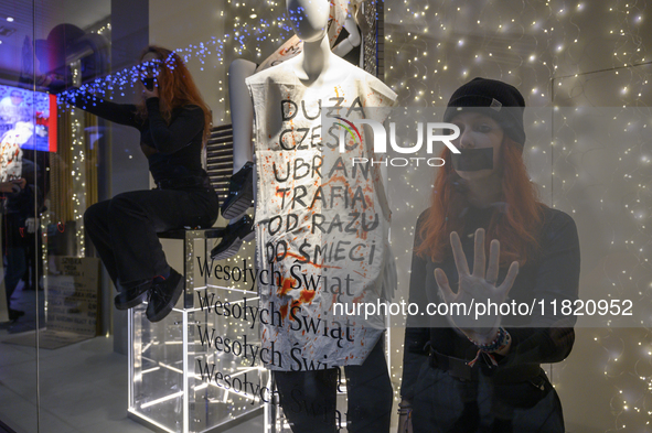 Climate activists with their hands glued to the shop window sit next to a mannequin that wears a message that reads ''The majority of clothe...