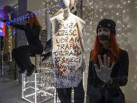 Climate activists with their hands glued to the shop window sit next to a mannequin that wears a message that reads ''The majority of clothe...