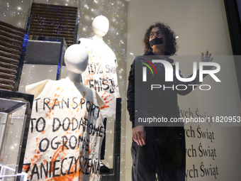 A climate activist with his hand glued to a shop window stands next to a mannequin that bears a message reading ''Transport is an additional...