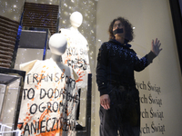 A climate activist with his hand glued to a shop window stands next to a mannequin that bears a message reading ''Transport is an additional...