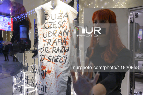 Climate activists with their hands glued to the shop window sit next to a mannequin that wears a message that reads ''The majority of clothe...