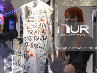 Climate activists with their hands glued to the shop window sit next to a mannequin that wears a message that reads ''The majority of clothe...