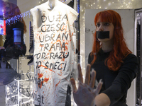 Climate activists with their hands glued to the shop window sit next to a mannequin that wears a message that reads ''The majority of clothe...