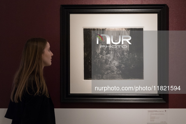 LONDON, UNITED KINGDOM - NOVEMBER 29, 2024: A staff member looks at print by Rembrandt Harmensz Van Rijn 'Christ crucified between the two T...