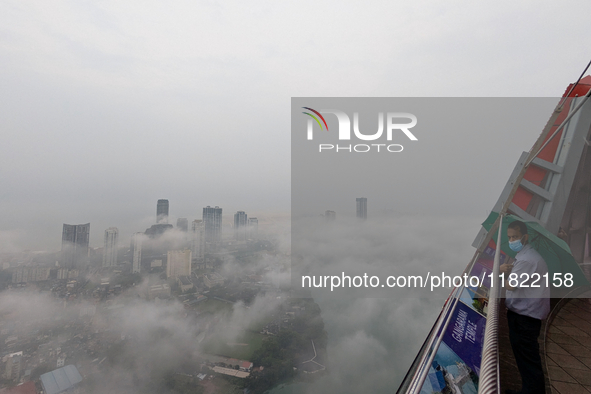 A man wearing a mask with an umbrella looks at the city of Colombo amid smog and rain from Lotus Tower in Colombo, Sri Lanka, on November 30...