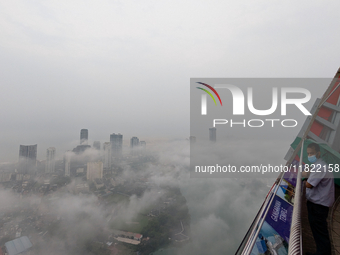 A man wearing a mask with an umbrella looks at the city of Colombo amid smog and rain from Lotus Tower in Colombo, Sri Lanka, on November 30...