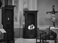 (EDITOR'S NOTE: Image was converted to black and white) A priest seated in a confessional, waiting in solitude in an empty church in Locorot...