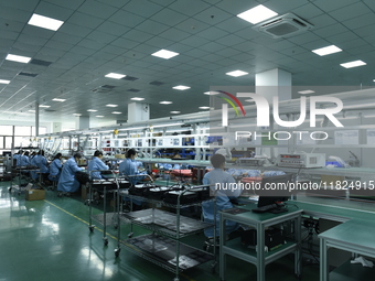 Workers install chips, resistors, and other components on a circuit board in a workshop in Fuyang, China, on November 30, 2024. (