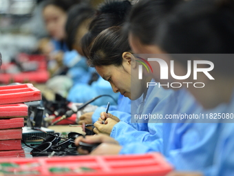 Workers install chips, resistors, and other components on a circuit board in a workshop in Fuyang, Anhui province, China, on November 30, 20...