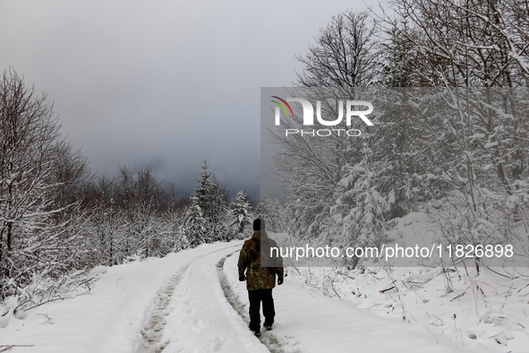 A tourist walks on a hiking trail amid picturesque views of Beskid Zywiecki as snow covers trees and the path. 