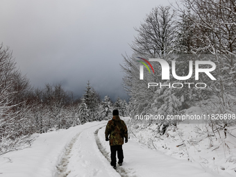 A tourist walks on a hiking trail amid picturesque views of Beskid Zywiecki as snow covers trees and the path. (