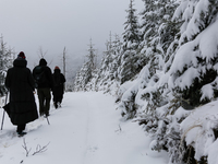 Tourists walk on a hiking trail amid picturesque views of Beskid Zywiecki as snow covers trees and the path. (