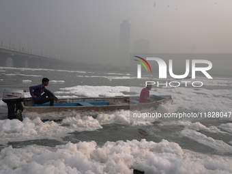 Workers for the Delhi water board move in a boat spraying defoaming chemicals to remove the toxic foam flowing in the Yamuna River in New De...