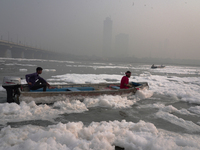 Workers for the Delhi water board move in a boat spraying defoaming chemicals to remove the toxic foam flowing in the Yamuna River in New De...