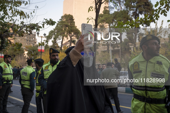 Iranian policemen stand guard outside the Turkish embassy while a veiled woman records video with her cellphone during a protest against Tur...