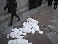 An Iranian protester walks past packages wrapped in shrouds symbolizing the bodies of people of Syria, which are placed on a sidewalk, durin...