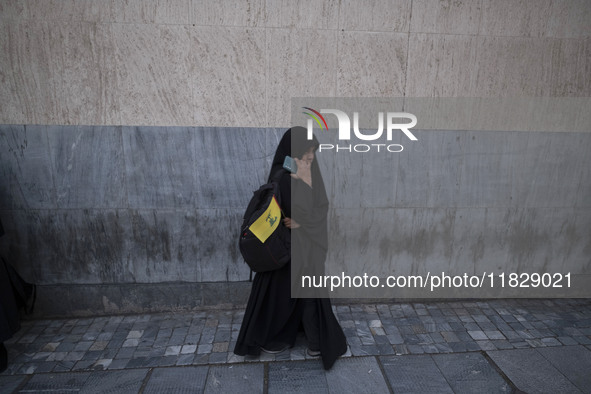 A veiled Iranian protester holds a flag of Lebanon's Hezbollah while standing on a sidewalk after a protest against Turkish President Recep...