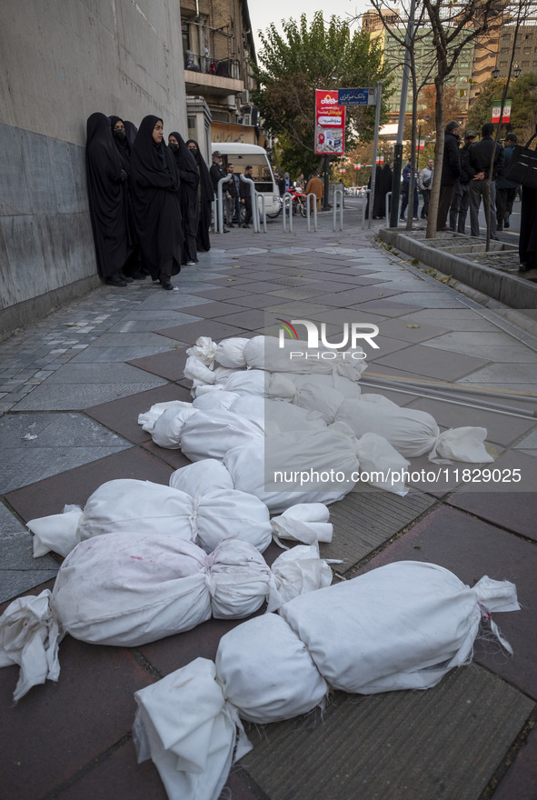 Veiled Iranian policewomen stand near packages wrapped in shrouds symbolizing the bodies of people of Syria, which are placed on a sidewalk,...