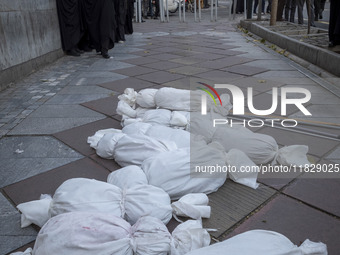 Veiled Iranian policewomen stand near packages wrapped in shrouds symbolizing the bodies of people of Syria, which are placed on a sidewalk,...