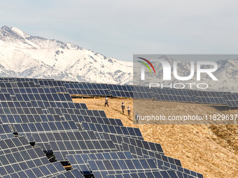 Workers of Huaneng Yili Xexin Photovoltaic Power Plant inspect equipment on a barren slope in Yili, Xinjiang province, China, on November 30...