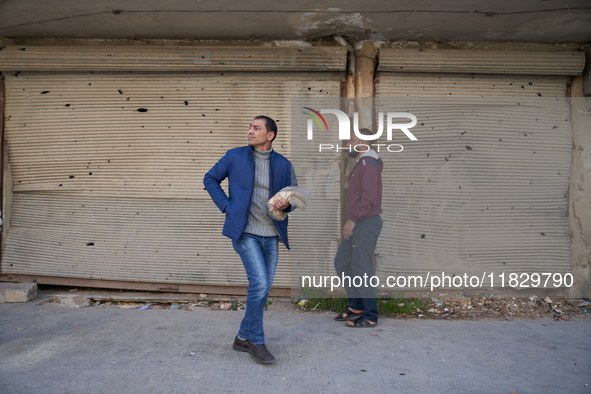 Two men walk past shops hit by shrapnel and bullets in the Bustan al-Qasr neighborhood in Aleppo, Syria, on December 1, 2024. 