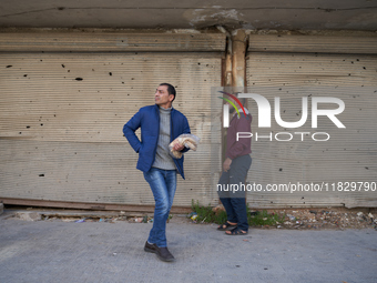 Two men walk past shops hit by shrapnel and bullets in the Bustan al-Qasr neighborhood in Aleppo, Syria, on December 1, 2024. (