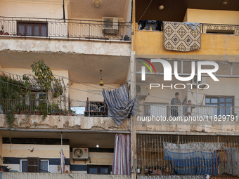 Residents stand on the balcony of their home in the Bustan Al Qasr neighborhood in Aleppo, on December 1, 2024 (