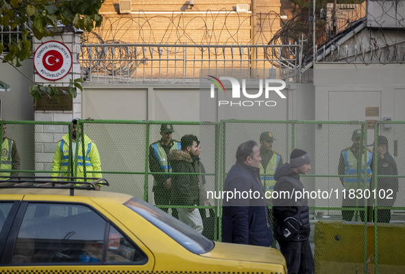 Iranian people walk past policemen guarding the Turkish embassy during a protest against Turkish President Recep Tayyip Erdogan and his dipl...