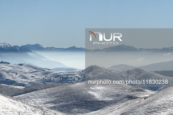 Snow-dusted rolling hills stretch toward distant mist-covered peaks in Campo Imperatore, Gran Sasso d'Italia, Italy, on November 16, 2024.  