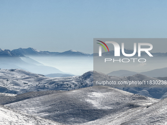 Snow-dusted rolling hills stretch toward distant mist-covered peaks in Campo Imperatore, Gran Sasso d'Italia, Italy, on November 16, 2024....