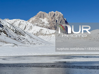 The frozen surface of a mountain lake reflects the Corno Grande under a blue sky in Campo Imperatore, Gran Sasso d'Italia, Italy, on Novembe...