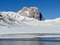 The frozen surface of a mountain lake reflects the Corno Grande under a blue sky in Campo Imperatore, Gran Sasso d'Italia, Italy, on Novembe...