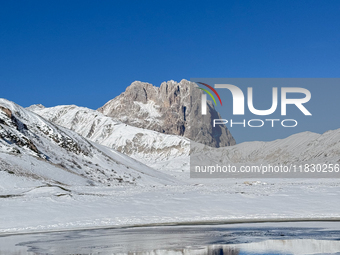 The frozen surface of a mountain lake reflects the Corno Grande under a blue sky in Campo Imperatore, Gran Sasso d'Italia, Italy, on Novembe...