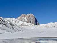 The frozen surface of a mountain lake reflects the Corno Grande under a blue sky in Campo Imperatore, Gran Sasso d'Italia, Italy, on Novembe...