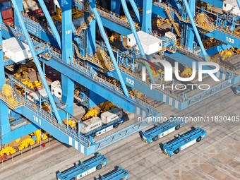 An automatic guided vehicle waits to deliver goods under a bridge crane at a fully automated terminal in Qingdao Port in Qingdao, China, on...